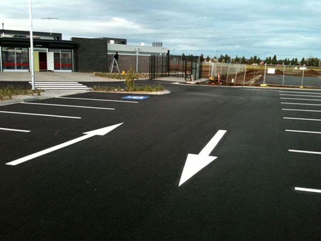White directional arrows and bay lines painted on new black asphalt in a car park outside a commercial building