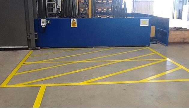 Yellow hatched keep-clear markings on a concrete floor in front of a blue loading door