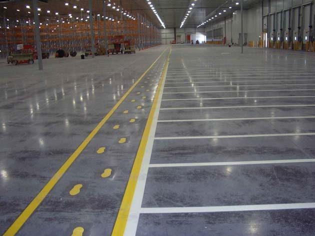 A yellow pedestrian walkway with painted footprints running the length of a polished warehouse floor