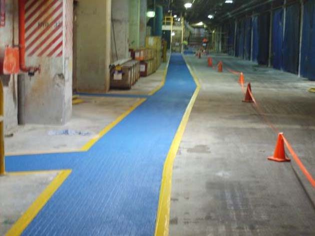 A blue anti-skid walkway with yellow edges through an industrial building