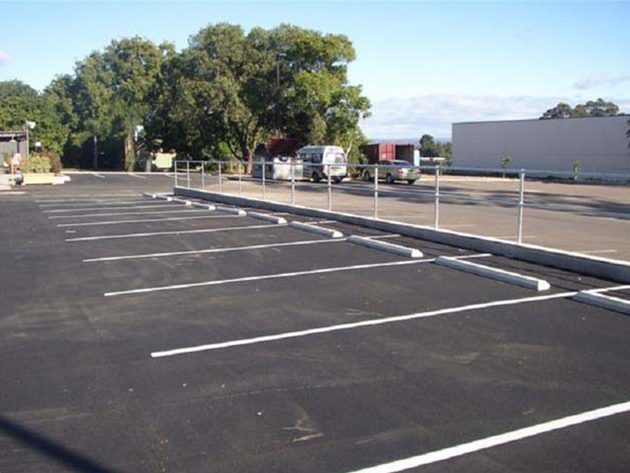 White parking bay lines and concrete kerbs on a new asphalt car park with vans parked beyond a fence