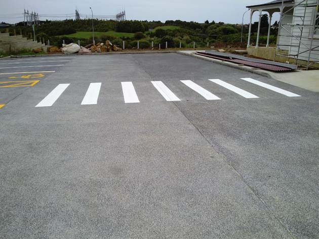 White pedestrian crossing stripes painted on a concrete yard beside a timber building