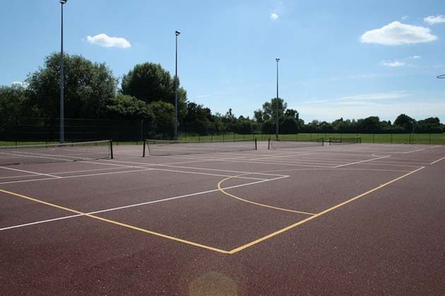 Tennis courts with a red surface, white and yellow lines and black nets under floodlight poles